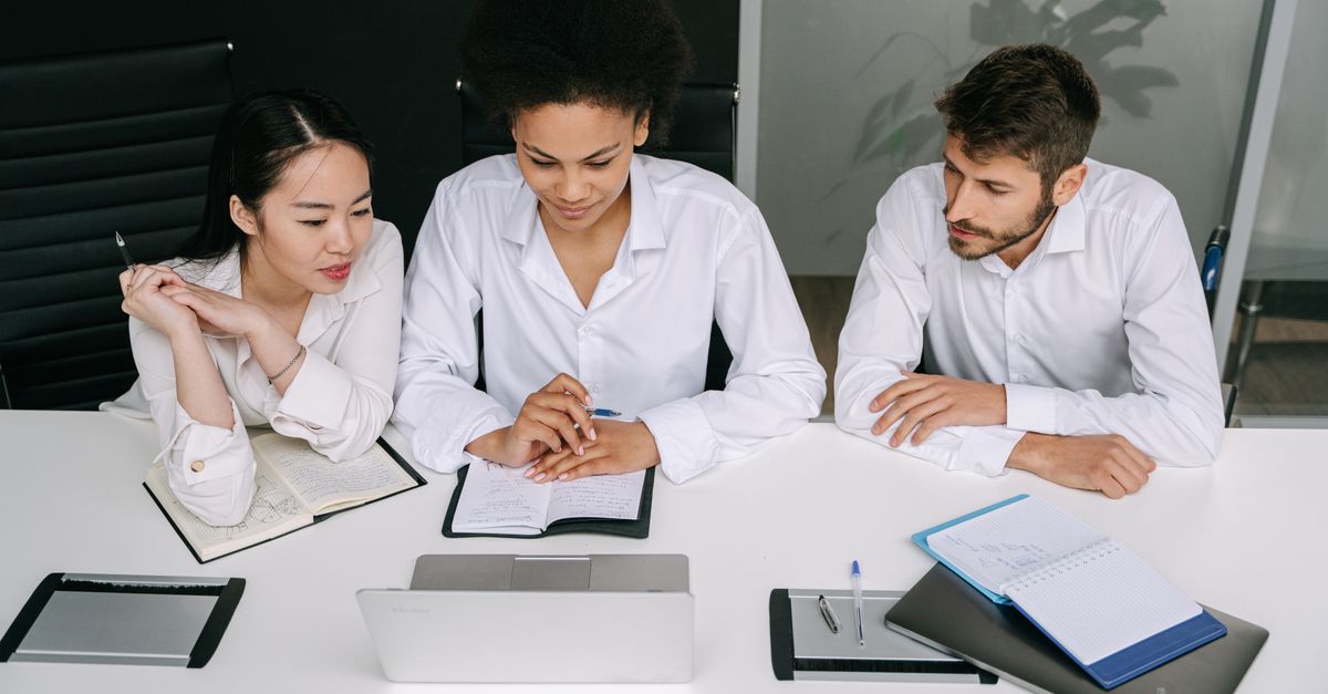 A diverse team collaborates in a modern office setting, focused on a laptop screen. Professional teamwork.