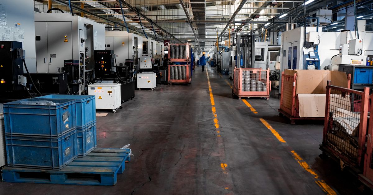 Vast industrial factory floor with machinery, crates, and structured workstations.